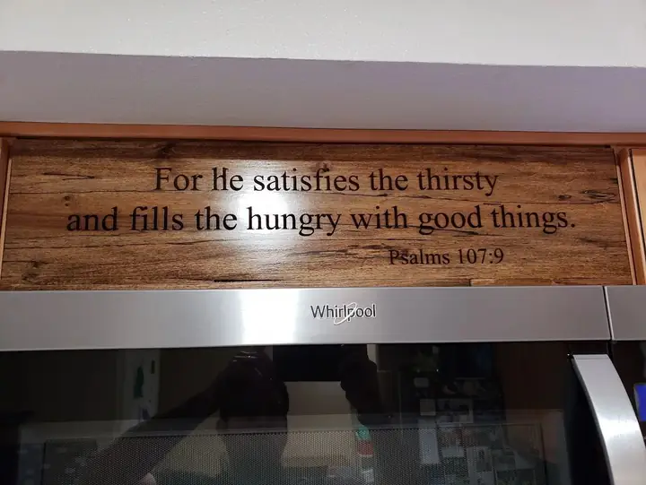 Wooden sign with an engraved verse above a microwave